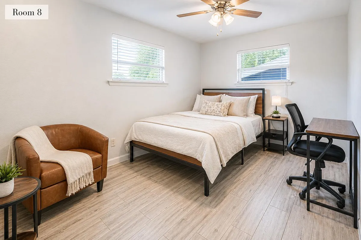Furnished bedroom with a full bed, two windows, ceiling fan, nightstand, and a dedicated desk workspace plus lounge chair. - Springwood Pl