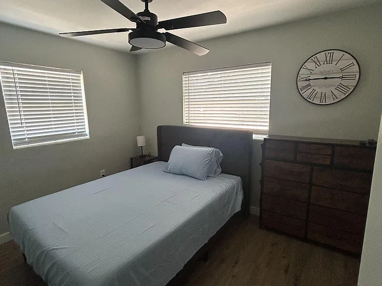 Furnished bedroom with a ceiling fan, two windows with blinds, and storage dresser for everyday convenience.
New mattress rep