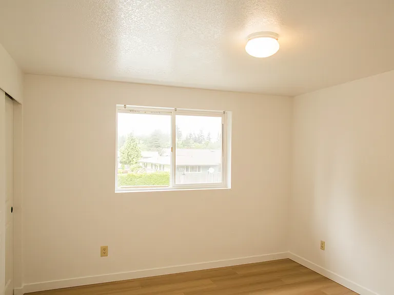 Bright bedroom with updated flooring, freshly repainted walls, and large window bringing in natural light. Comfortable and clean living space with peaceful neighborhood views.