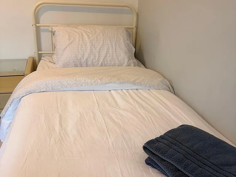 Private bedroom setup with a twin bed, metal headboard, and convenient bedside surface for personal items.