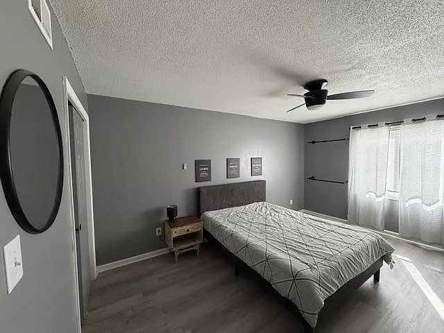 Spacious bedroom with a ceiling fan, large window with curtains, and a comfortable bed setup with side table.