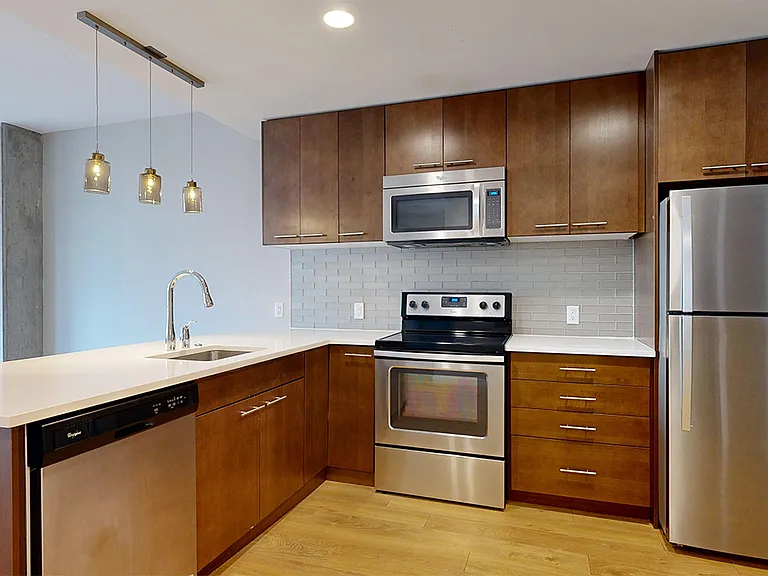 Apartment kitchen with stainless steel appliances, quartz countertops and wood-style flooring.
