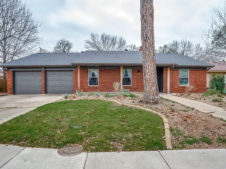Brick facade residence featuring a dark shingle roof and a two-car garage with gray doors