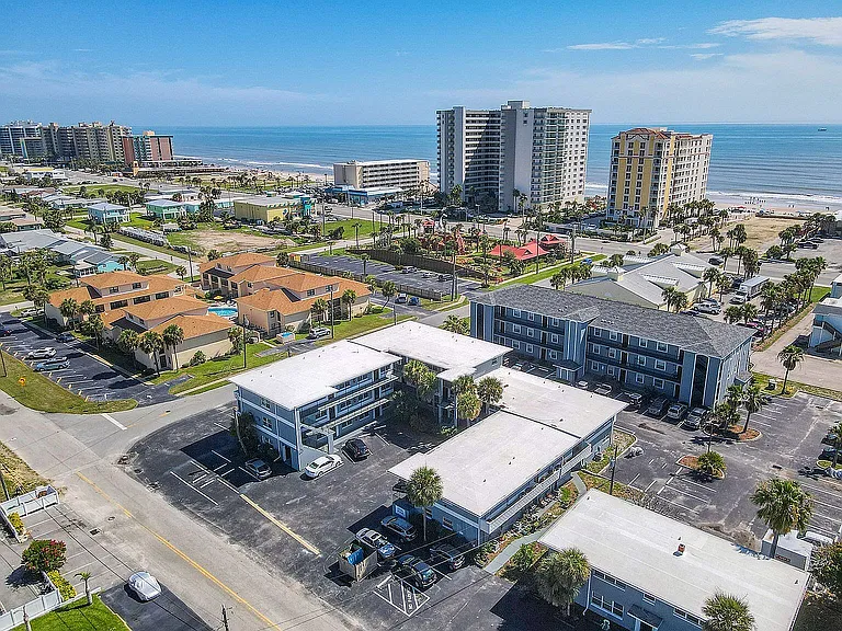 Stunning aerial view of a vibrant coastal community featuring modern apartment buildings with ocean views, lush greenery, and easy beach access.