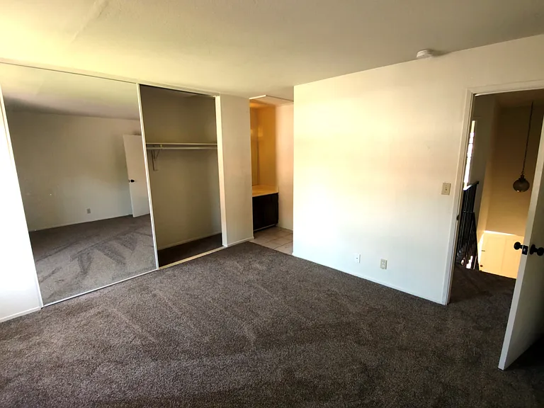 Primary bedroom, taken from the corner opposite the bathroom. Large closet with mirror doors, in-room vanity sink, and direct access to the bathroom.