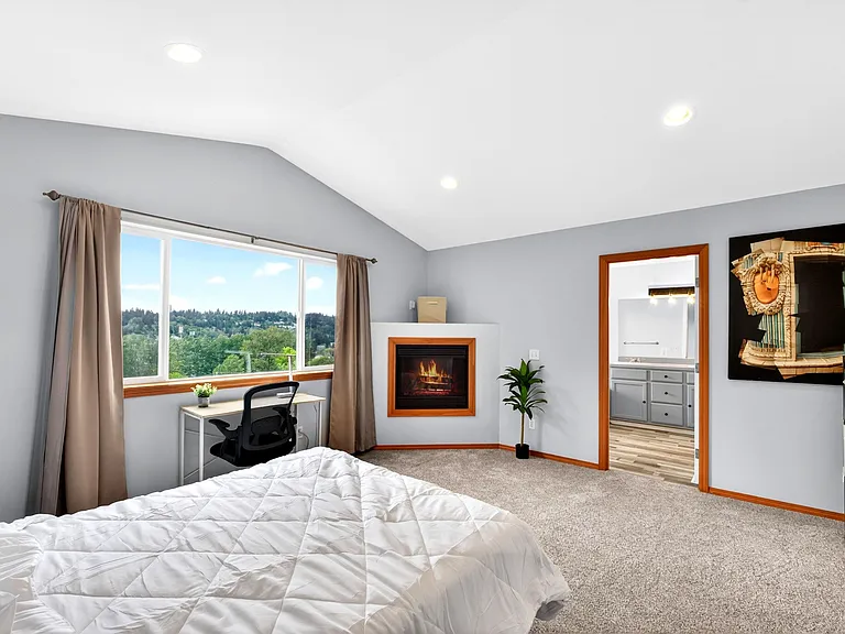 Spacious bedroom with large picture window, desk nook, and an in-room fireplace; direct access to an adjacent bathroom.