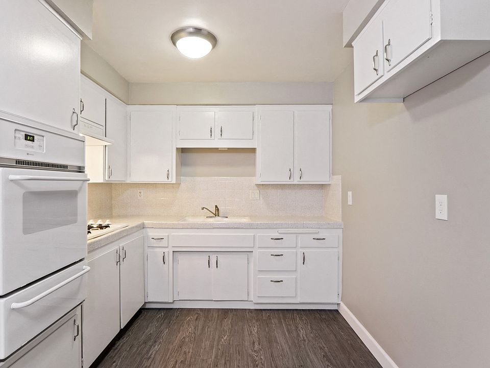 Kitchen with White oven, cooktops on the left, double white kitchen sink, white kitchen cabinets and cupboards, Tile backsplash and countertops, wood style flooring