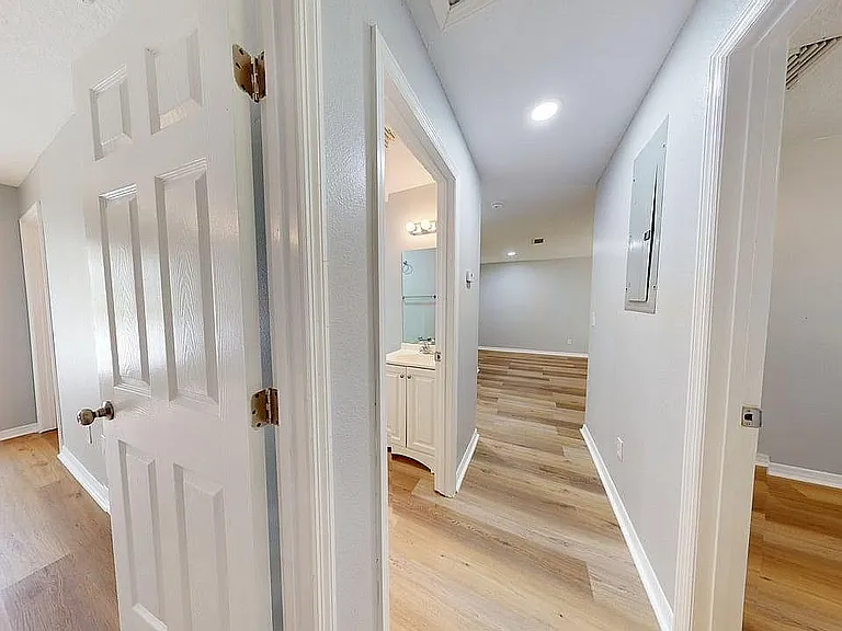Inviting apartment hallway with stylish wood flooring, directing toward a bright living space and modern bathroom.
