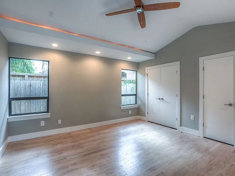 Vaulted master bedroom showing the cove-lit recessed ceiling, dual closets, and twin windows with sideyard view