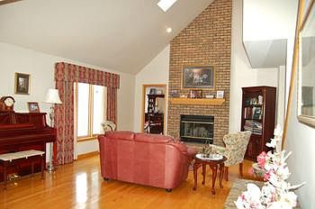 Living room with wood flooring and fireplace has vaulted ceilings.