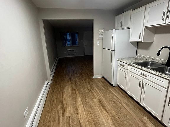Modern kitchen with sleek granite countertops, white cabinetry, and warm wood flooring extending into a cozy living area.