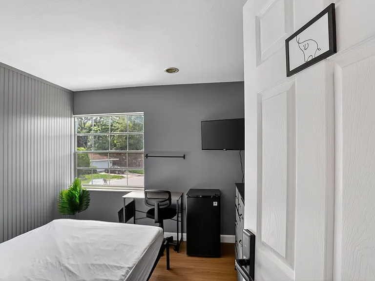 Private bedroom with a large window, dedicated desk workspace, wall-mounted TV, and in-room mini fridge for added convenience