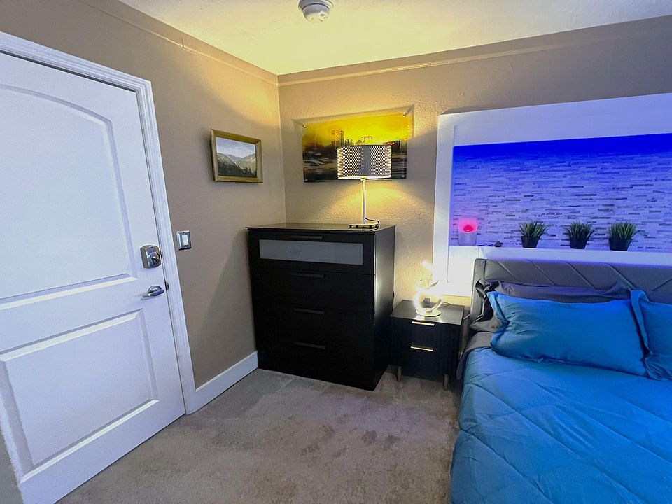 Furnished bedroom with a comfortable bed, nightstand lighting, and dresser storage, plus a decorative recessed accent wall.