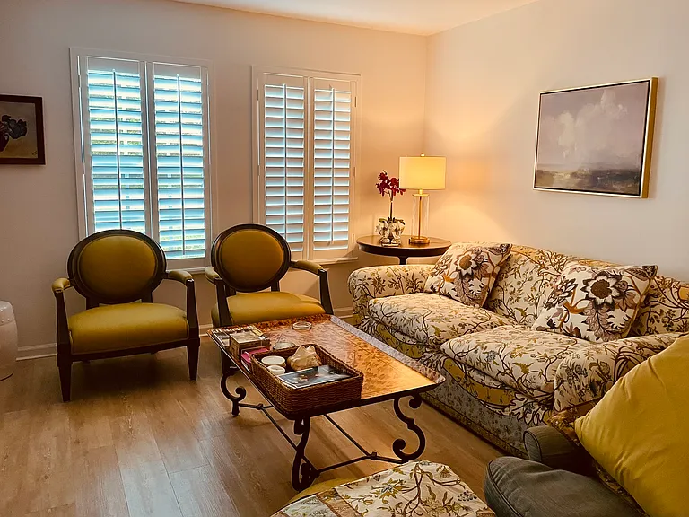 A sophisticated and light-filled main living area featuring traditional designer furniture, polished flooring, and upscale plantation shutters. A pristine elegant, well-maintained home environment.