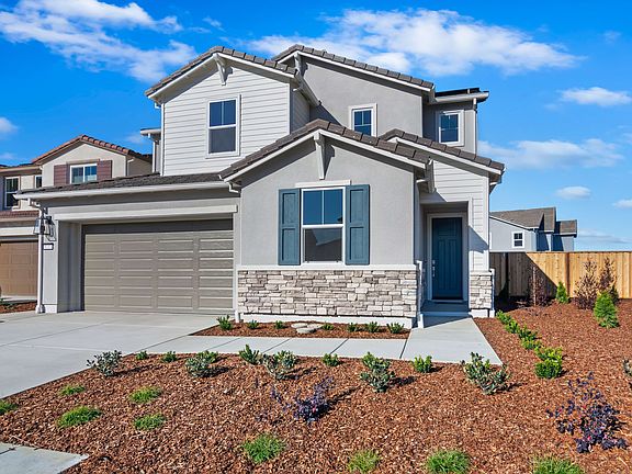 A modern two-story house with a garage, surrounded by a landscaped yard with plants and a clear blue