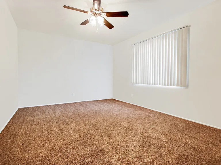 Bedroom with carpeted floors, ceiling fan and vertical window blinds on the right