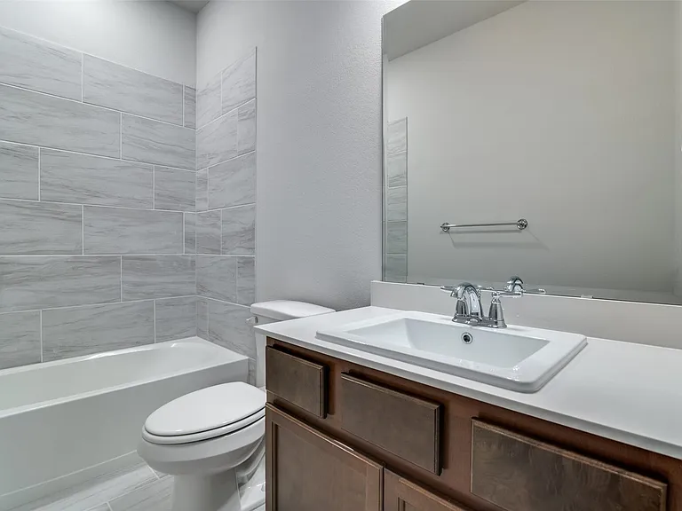 Full bathroom featuring a rectangular drop-in sink with chrome faucet, a white countertop, wood-finish cabinetry, and a tub with light-toned tiled surround