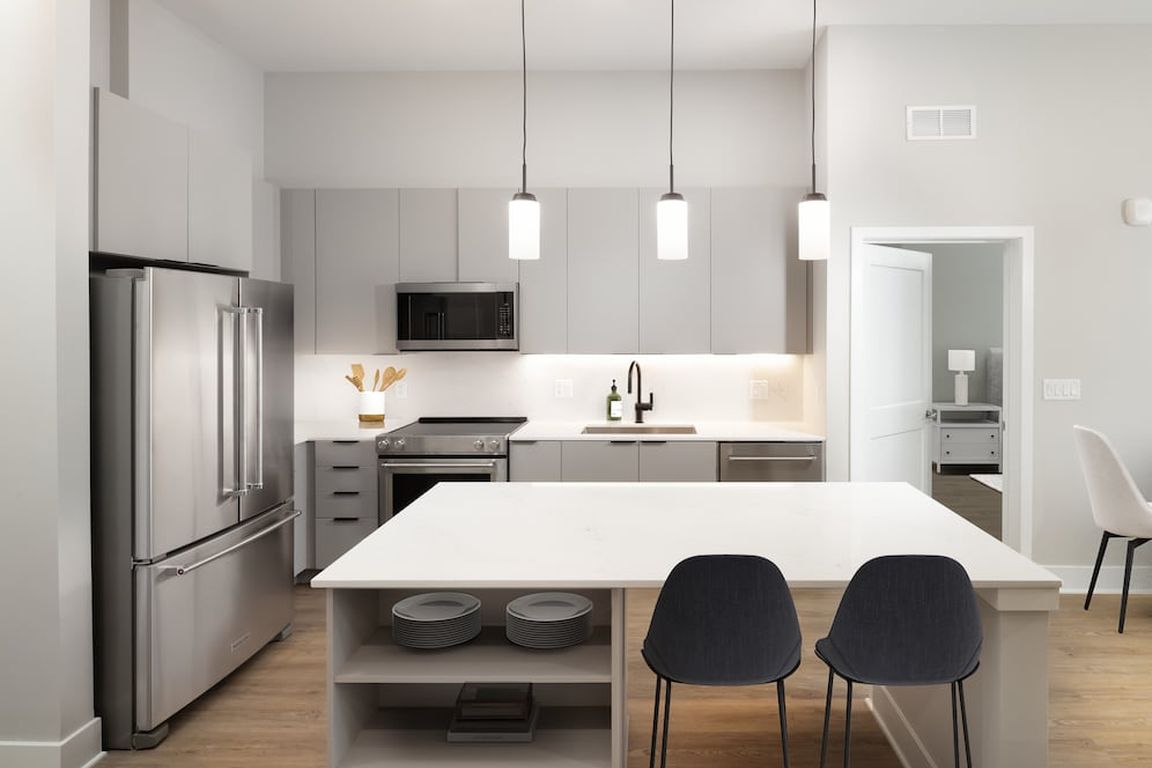 Signature Collection kitchen with stainless steel appliances, light grey cabinetry, marbled quartz countertops and backsplash, under-cabinet lighting, built-in shelves, and hard-surface flooring
