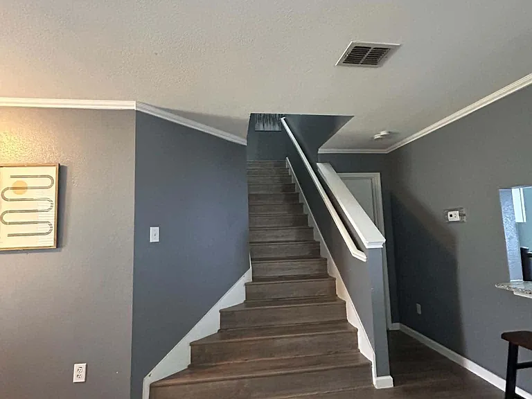 Open entry area with wood-look floors and a staircase featuring a sturdy handrail for easy access to upper rooms.