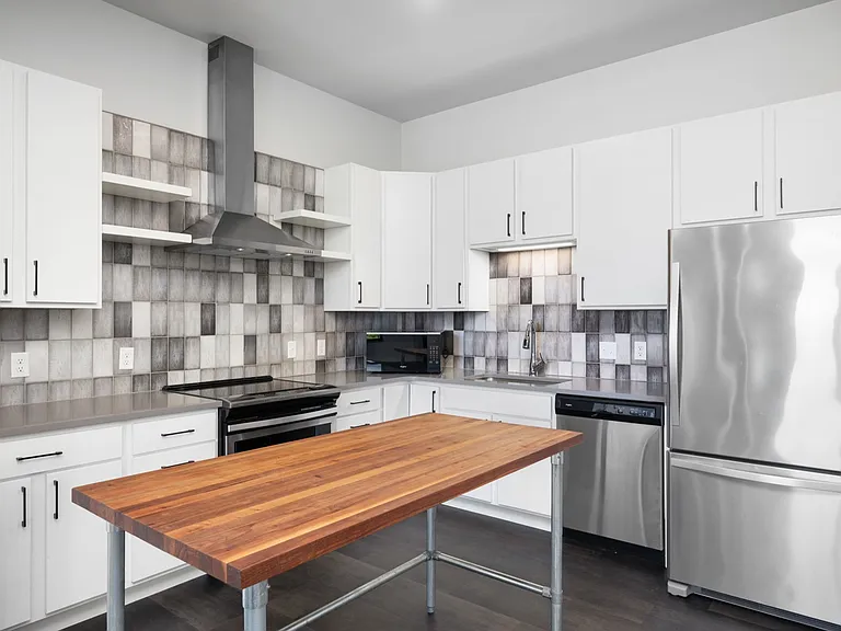 Modern kitchen featuring sleek stainless steel appliances, white cabinetry, and a chic wooden island accenting the contemporary tile backsplash. Modern kitchen featuring sleek stainless steel appliances, white cabinetry, and a chic wooden island accenting