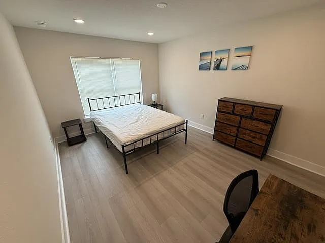 Spacious bedroom with a metal bed frame, large window with blinds, and ample room for a dresser and desk.