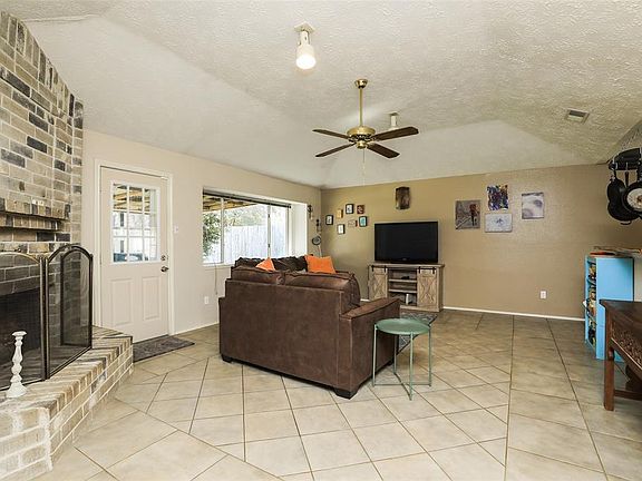 Spend countless hours in this large living room featuring ceramic tile, cove ceiling, neutral paint with warm-colored accent wall, ceiling fan, and decorative baseboards