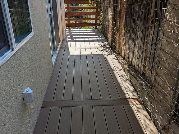Private deck with modern plank flooring and a secure perimeter. This peaceful retreat includes a dedicated pet area and stunning views of the valley mountain range_perfect for enjoying summer sunsets with your furry friend. Plenty of room for seating.