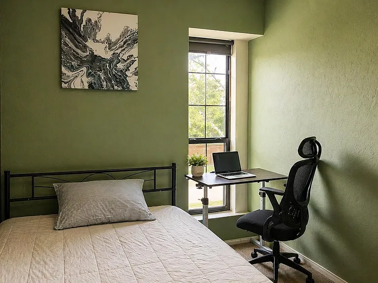 Private bedroom with a comfortable bed, dedicated desk workspace, and a large window bringing in natural light.