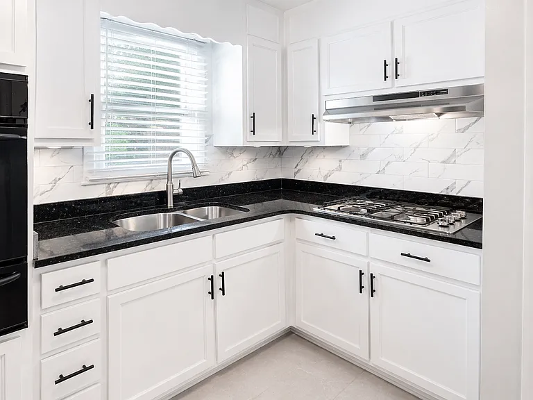 Updated kitchen featuring a new stainless steel cooktop, granite countertops, refrigerator, and sink.