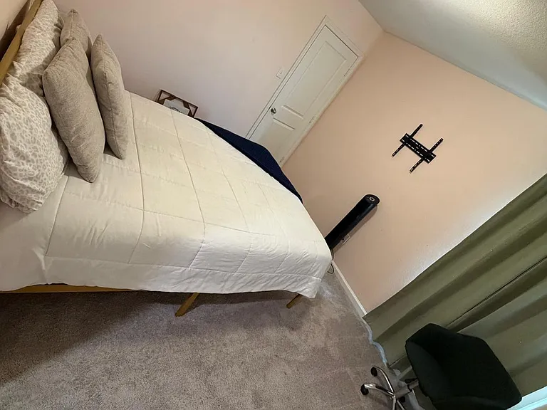 Carpeted bedroom with a queen bed setup, neutral walls, and space for a desk or seating, plus a TV-mount ready wall.