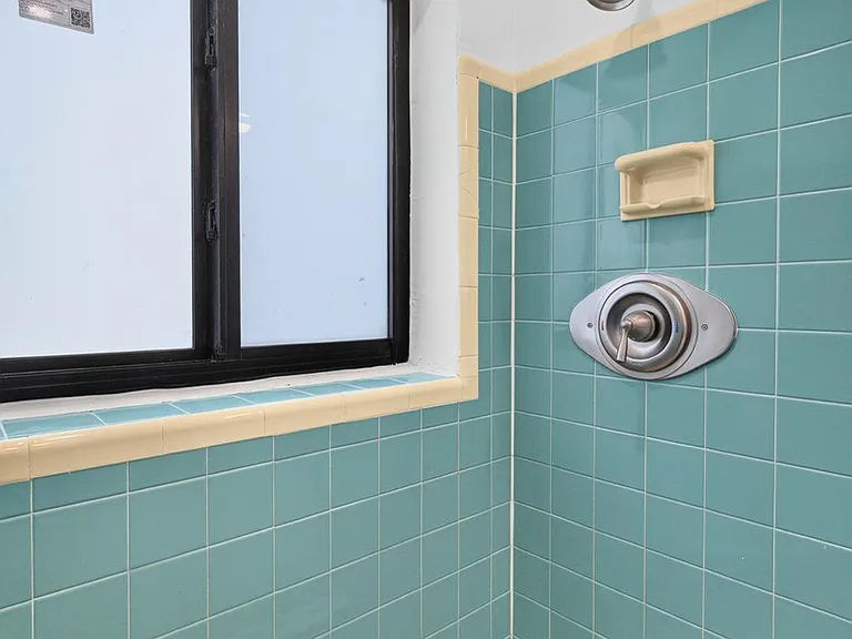 Tiled shower stall with built-in soap dish, adjustable showerhead, and a frosted window for added privacy.