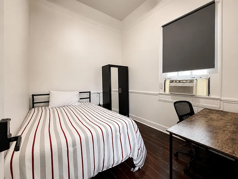 Private furnished bedroom featuring a bed, wardrobe storage, and a dedicated desk area with window A/C.