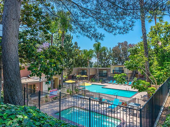 Outdoor swimming pool area with sundeck and lounge seating surrounded by foliage.