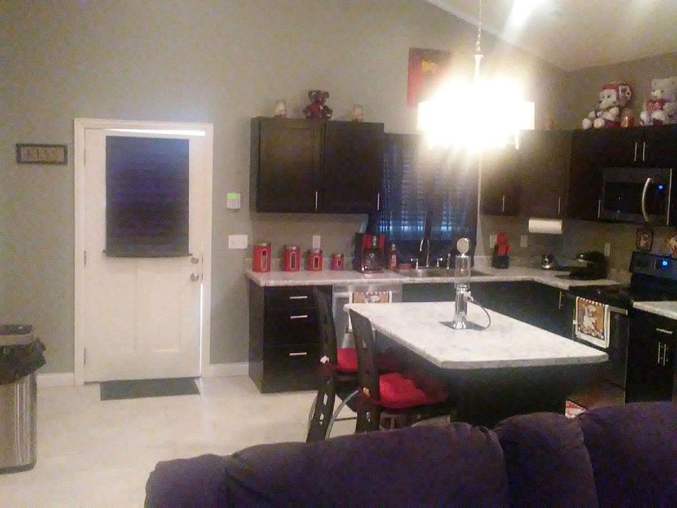 Kitchen area with center island and full appliances including refrigerator, oven, microwave, dishwasher. Laundry room to the left includes stackable washer and dryer. Note the lofted ceilings and light fixtures.