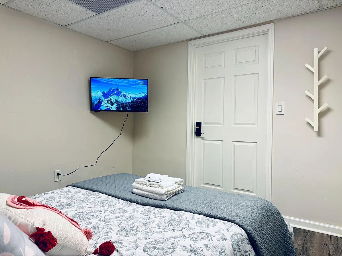 Furnished bedroom with a comfortable bed, wall-mounted TV, and door-side wall hooks for everyday convenience. - Wyntercreek Dr