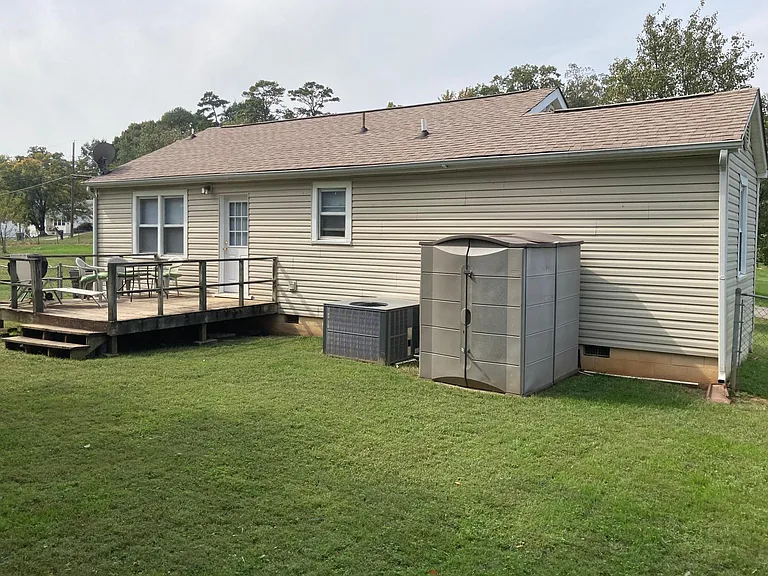 Back yard with deck, AC unit and storage shed for lawn mower and garden tools.