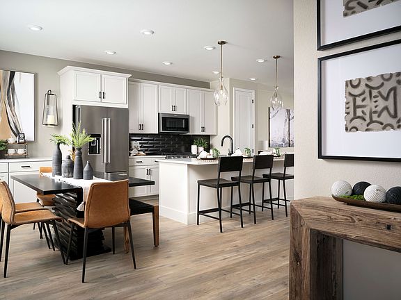 A modern, open-concept kitchen and dining area with white cabinets, stainless steel appliances, a wo