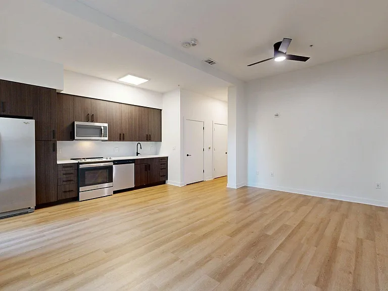 Apartment kitchen with stainless steel appliances, dining and living room with wood-style flooring.