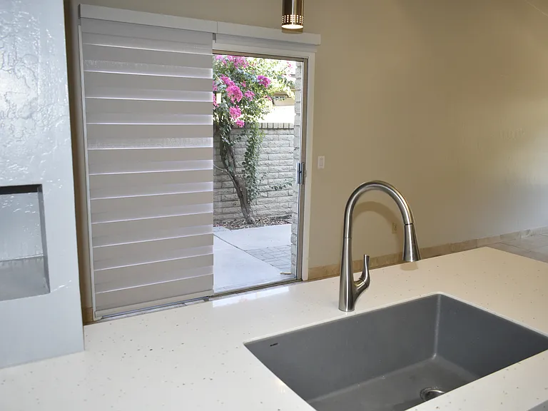 View of Kitchen sink and patio door from inside kitchen - Solid-surface countertops with single basin sink and faucet with retractable spray head.