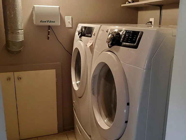 View of high-efficiency washer and dryer in laundry room. Sprinkler system on the wall. Doors access crawl space/furnace.