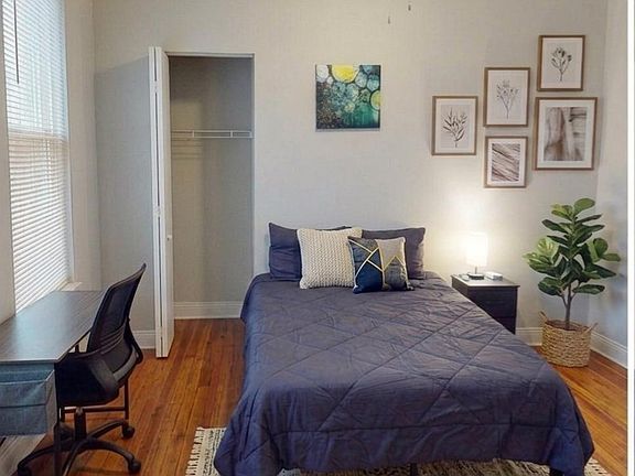 Furnished bedroom with a full-size bed, hardwood floors, a desk workspace, and an open closet for easy storage.