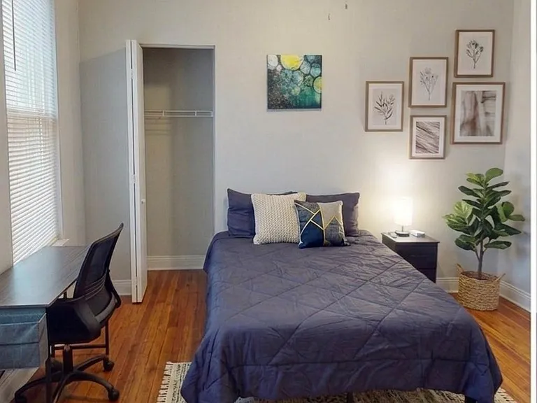Furnished bedroom with a full-size bed, hardwood floors, a desk workspace, and an open closet for easy storage.