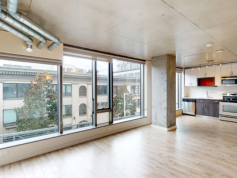 Apartment kitchen with stainless steel appliances, dining and living room with wood-style flooring.