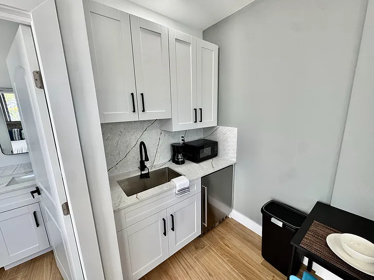 Compact kitchenette with shaker cabinets, stone-look counters/backsplash, undermount sink, and under-counter fridge.