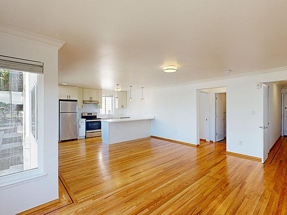 Spacious living room with a wood-like flooring, large windows, and a view of the kitchen