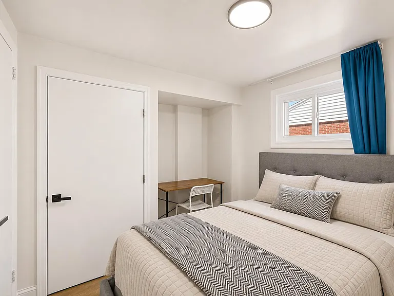 Furnished bedroom with a full bed, dedicated desk nook, and a window with curtain panel for natural light.