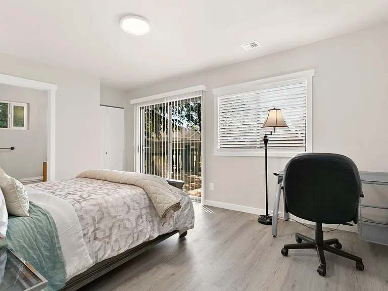 Bedroom with a full bed, desk setup, and large windows plus a sliding glass door for easy outdoor access.