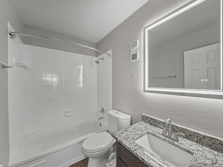 Updated two-bedroom apartment bathroom with granite vanity and modern lighting