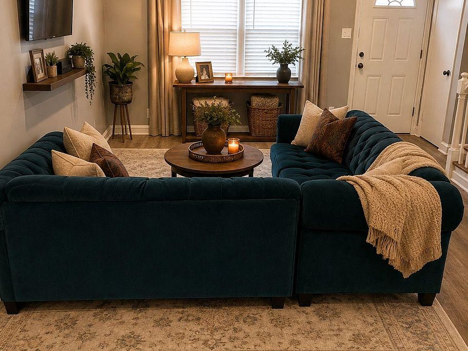 Inviting living area with a sectional seating layout, wall-mounted TV, and a large window with blinds and drapes.