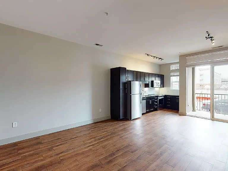 Apartment kitchen with stainless steel appliances, dining and living room with wood-style flooring.